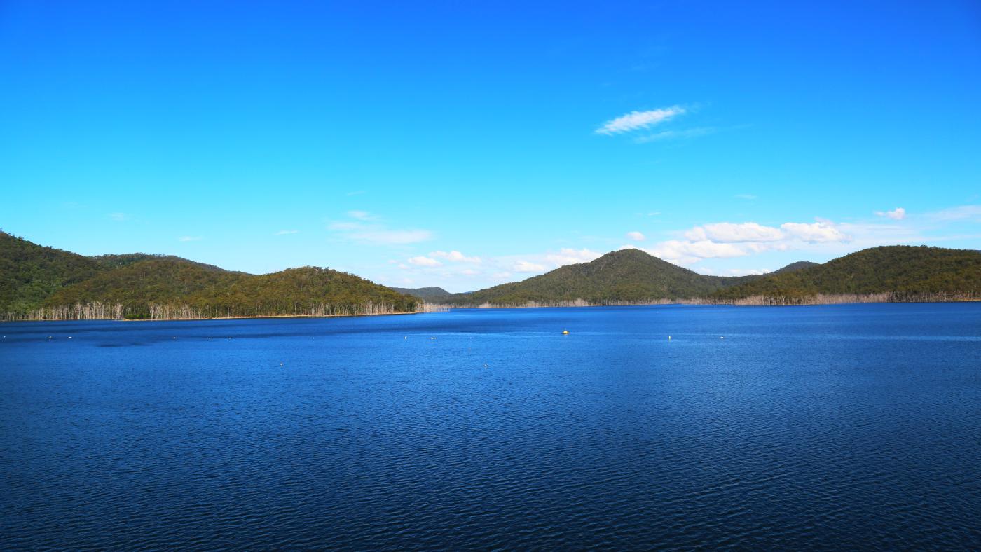 A deep blue lake with hilly green forest in the distance on a sunny day