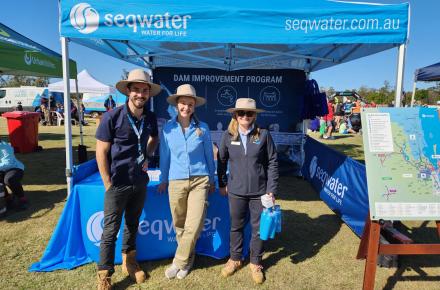 Three Seqwater workers standing in front from a branded marquee smiling