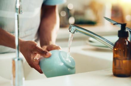 Person washing dishes at sink with tap running