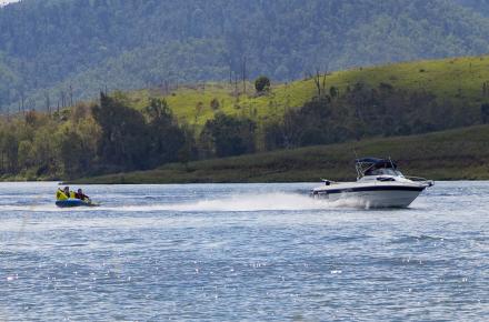 A wide angled photo of white boat pulls two people on an inflatable towards right of screen