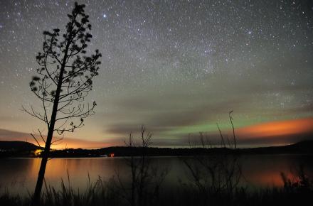 Twinkling stars shine over a calm lake with a hint of orange sunset in the background