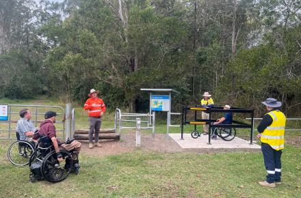 One person using a wheelchair uses the new gate at Ewen Maddock, watched on my three people standing and two people using wheelchairs