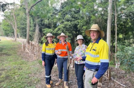 Four people in hi vis workwear stand in front of a native plant riverbank revegetation project