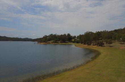 Image of the shoreline of Wivenhoe Dam, calm blue lake meets short green grass