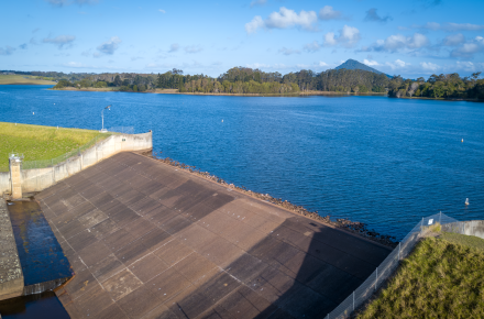 Drone shot of a crystal blue lake with a wide concrete spillway